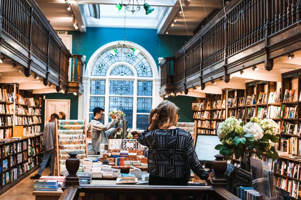 Inside of a bookshop, with customers perusing shelves and a glass window straight ahead. books author bookstagram social media writing reading