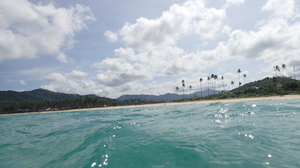 Nacpan Beach shown from the blue waters, with clouds and palm trees in the background.Lesser known underrated travel destinations to add to your itinerary solo female travel