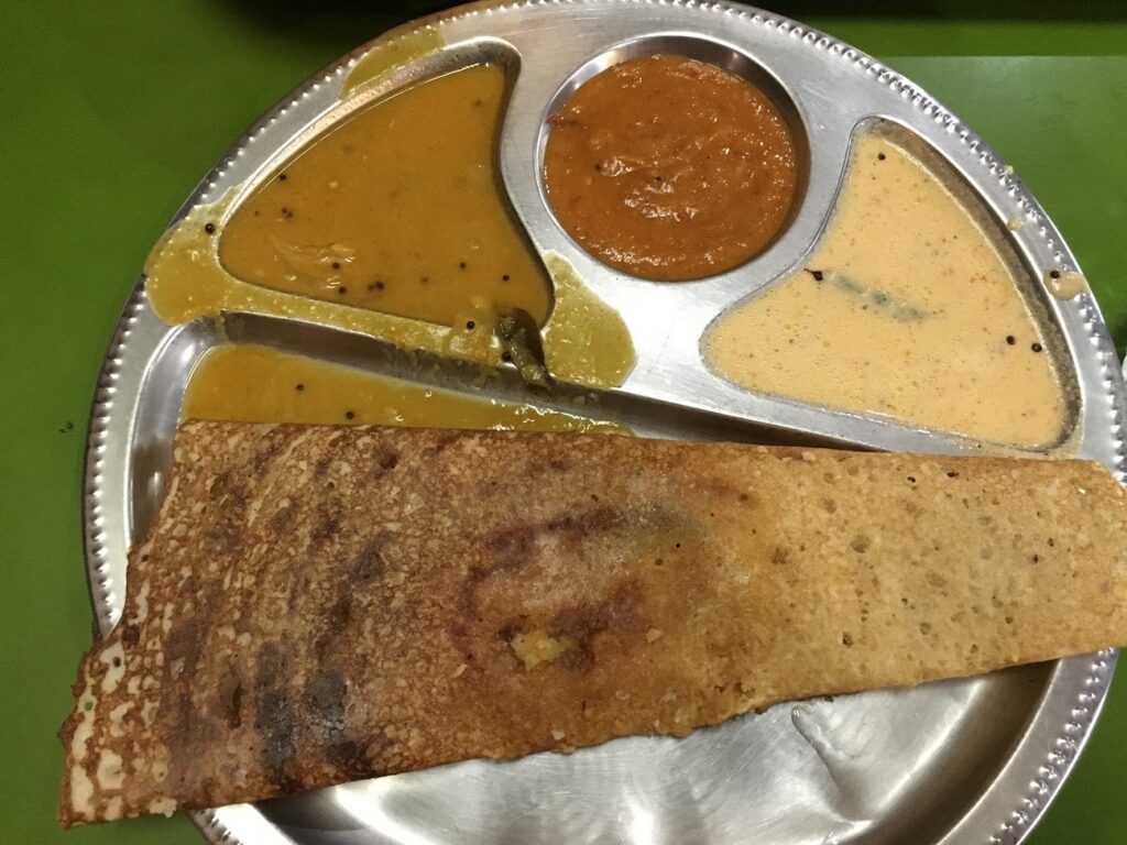 A metal plate with a dosa on the bottom and three chutneys in various shades of orange on top. Lesser known underrated travel destinations to add to your itinerary solo female travel